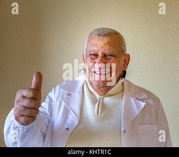 Alte Doktor mit Flecken auf der Stirn lächelnd und mit Daumen hoch Stockfoto