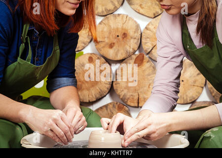 Eine junge Frau potter lehrt eine rothaarige Frau auf töpferscheibe ein Vase braun Ton in einem kreativen Workshop in grün Stil, Seitenansicht modellieren Stockfoto