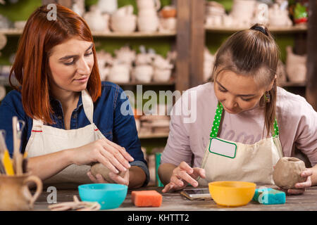 Frau Töpfer hält eine Lektion rothaarige Frau eine Lektion in Keramik und zeigt am Telefon ein Bild von Ton Ware in einem schönen Werkstatt, in der backgrou Stockfoto