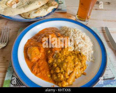 Indische Speisen zum Mitnehmen serviert zu Hause Chicken Madras Curry, Tarka Dahl, Tandoori Naan Brot, Basmati Reis, Mango und Limette Chutney. s und ein Glas o Stockfoto