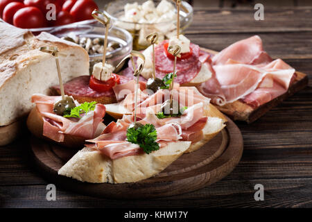 Spanische Tapas mit Scheiben Jamon Serrano, Salami, Oliven und Käse Würfeln auf einem Holztisch. Spanische Küche Stockfoto