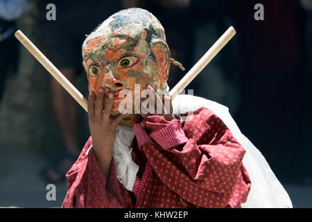 Ein kleiner buddhistischer Mönch in einem antiken Maske mit Gesicht eines Mannes, einer alten Gewand und Sticks in den Händen, eine tibetische alte Zeremonie. Stockfoto