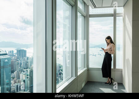 Business Woman in Wolkenkratzer office Fenster mittels Smartphone Stockfoto
