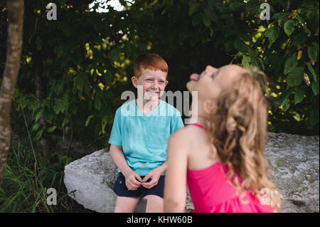 Mädchen kleben die Zunge raus Bruder sitzt auf Felsen Stockfoto