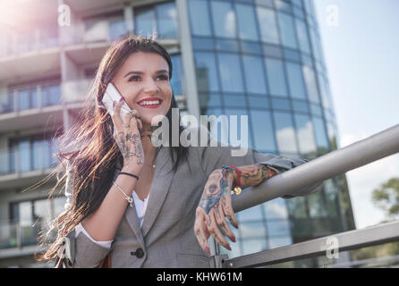 Geschäftsfrau im Freien, mit Smartphone, lächelnd, Tattoos auf Händen Stockfoto
