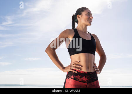 Junge Läuferin am Strand mit den Händen auf den Hüften gegen den blauen Himmel Stockfoto