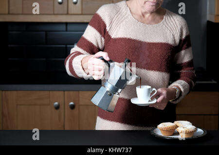 Ein smart, aber leger gekleidete Frau gießen einen Espresso aus einer molaren Herd Espressomaschine während Stehen in Ihrer Küche zu Hause. Stockfoto