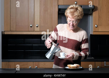 Ein smart, aber leger gekleidete Frau gießen einen Espresso aus einer molaren Herd Espressomaschine während Stehen in Ihrer Küche zu Hause. Stockfoto