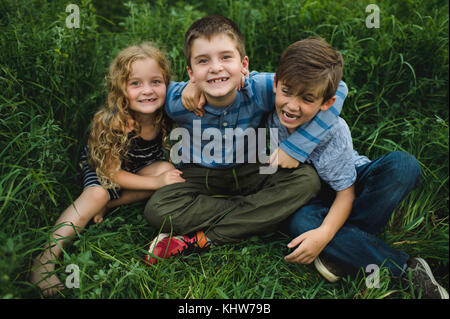 Brüder und Schwester genießen im Freien auf der grünen Wiese Stockfoto