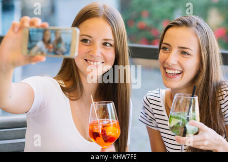 Zwei junge weibliche Freunde, Smartphone selfie im Straßencafé Stockfoto