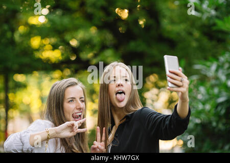 Zwei junge weibliche Freunde Grimassen für Smartphone selfie in Park Stockfoto