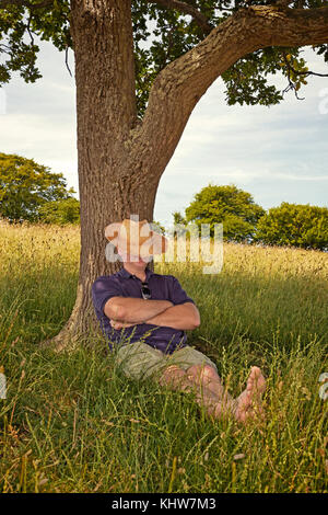 Ein Mann, ein Nickerchen im Schatten eines alten Baumes an einem heißen sonnigen Sommertag. Stockfoto