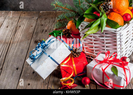 Weihnachten und Neujahr Konzept. frische Tangerinen mit grünen Blättern in einem weissen Korb, Weihnachtsdekoration und Geschenkboxen, auf alten rustikalen Holztisch, Stockfoto