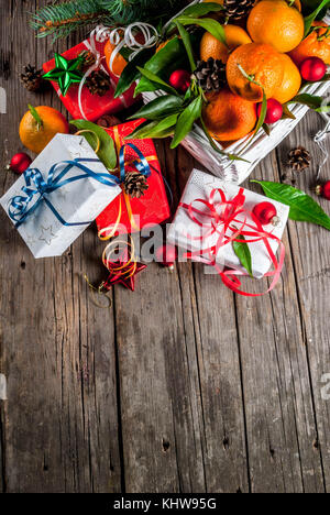 Weihnachten und Neujahr Konzept. frische Tangerinen mit grünen Blättern in einem weissen Korb, Weihnachtsdekoration und Geschenkboxen, auf alten rustikalen Holztisch, Stockfoto