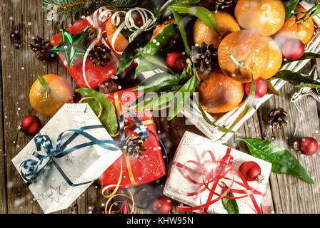 Weihnachten und Neujahr Konzept. frische Tangerinen mit grünen Blättern in einem weissen Korb, Weihnachtsdekoration und Geschenkboxen, auf alten rustikalen Holztisch, Stockfoto