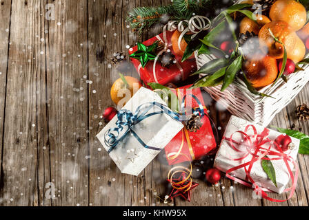 Weihnachten und Neujahr Konzept. frische Tangerinen mit grünen Blättern in einem weissen Korb, Weihnachtsdekoration und Geschenkboxen, auf alten rustikalen Holztisch, Stockfoto