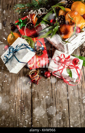 Weihnachten und Neujahr Konzept. frische Tangerinen mit grünen Blättern in einem weissen Korb, Weihnachtsdekoration und Geschenkboxen, auf alten rustikalen Holztisch, Stockfoto