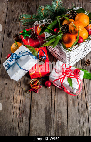 Weihnachten und Neujahr Konzept. frische Tangerinen mit grünen Blättern in einem weissen Korb, Weihnachtsdekoration und Geschenkboxen, auf alten rustikalen Holztisch, Stockfoto