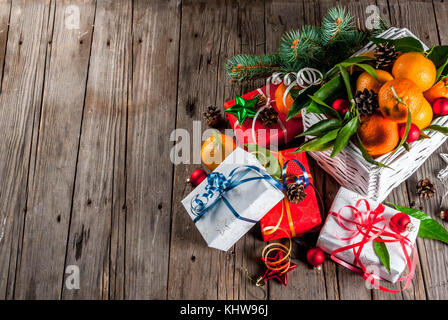 Weihnachten und Neujahr Konzept. frische Tangerinen mit grünen Blättern in einem weissen Korb, Weihnachtsdekoration und Geschenkboxen, auf alten rustikalen Holztisch, Stockfoto