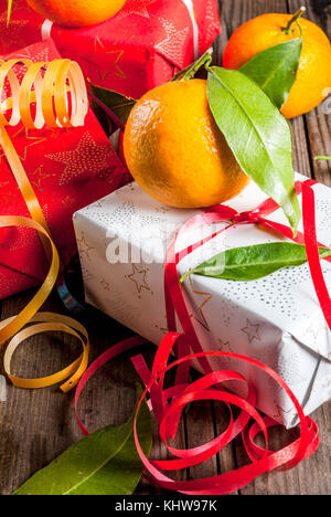 Weihnachten und Neujahr Konzept. frische Tangerinen mit grünen Blättern in einem weissen Korb, Weihnachtsdekoration und Geschenkboxen, auf alten rustikalen Holztisch, Stockfoto