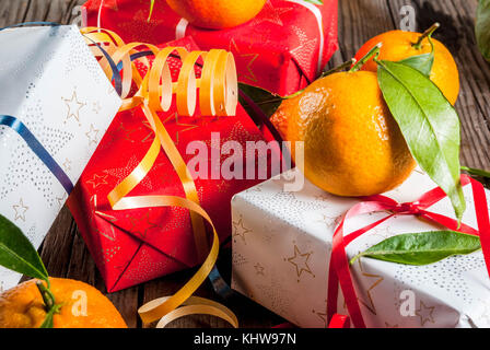 Weihnachten und Neujahr Konzept. frische Tangerinen mit grünen Blättern in einem weissen Korb, Weihnachtsdekoration und Geschenkboxen, auf alten rustikalen Holztisch, Stockfoto