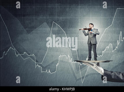 Geschäftsmann auf Metall Fach Violine spielen gegen konkreten Hintergrund mit Diagrammen Stockfoto