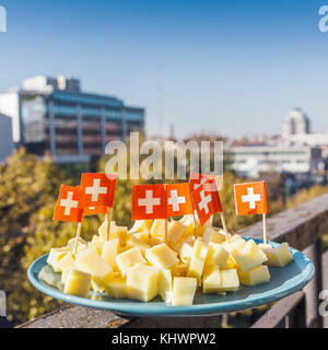 Emmentaler Käse mit Schweizer Flagge auf Zahnstochern - grüner sonniger Stadtgrund Stockfoto