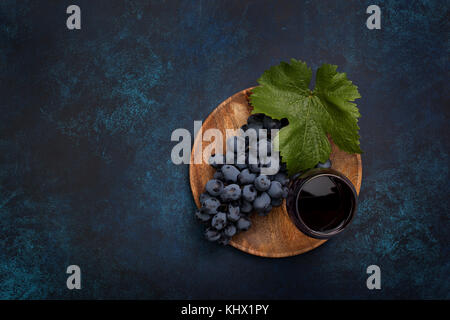 Weintraube und einem Glas Rotwein auf einer Holzplatte auf einem blauen Hintergrund. Ansicht von oben Stockfoto