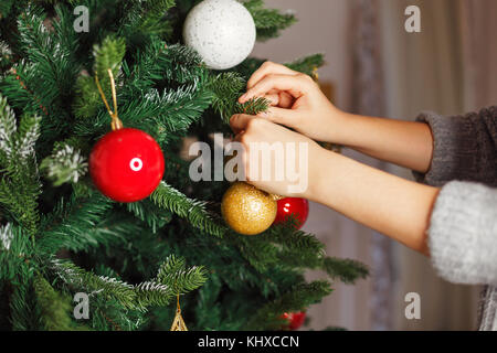 Das Mädchen schmückt den Weihnachtsbaum für den Urlaub. schießen. Kugeln und andere Dekorationen. Stockfoto