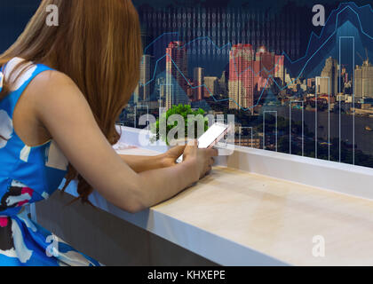 Frau mit dem Handy auf dem Sitz mit trading Graph im Stadtbild bei Nacht Hintergrund, Shopping online mit digital Laptop, Technologie und Stockfoto