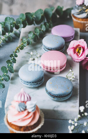 Pastellfarben Macarons, kleine Kuchen und Blumen auf Marmor Hintergrund. Hochzeit Süßigkeiten, Hochzeit Cupcakes und Makronen. Selektiver Fokus Stockfoto