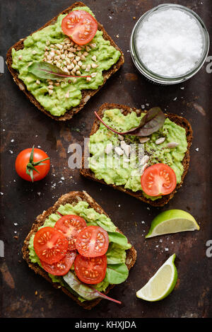 Nützliche avocado Toasts mit Sprossen, Tomate, Samen und Meer Salz Flocken. Tabelle Draufsicht, vertikal Stockfoto