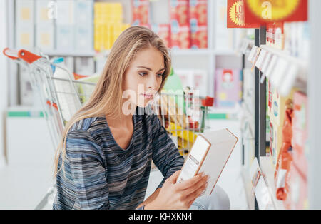 Junge Frau, Einkaufen im Supermarkt und Lesen von Lebensmitteln mit Zutaten auf einem Kasten, Einkaufen und Ernährung Konzept Stockfoto