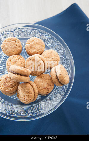 Lady's Kisses (Gebäck Gebäck mit Mandeln und Schokolade) auf Glas Kuchen steht gearbeitet. blau Preußen Tischdecke als Hintergrund. Stockfoto