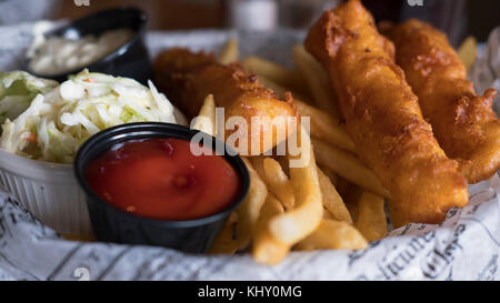 Die Anzeige der leckeren Fisch und Chips, Krautsalat und Salsas im englischen Stil auf einem Teller mit Zeitung Schnitten bedeckt serviert. Stockfoto