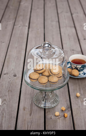 Lady's Kisses - italienische Haselnuss sandwich Cookies auf Kuchen stand mit einer Tasse Tee Stockfoto