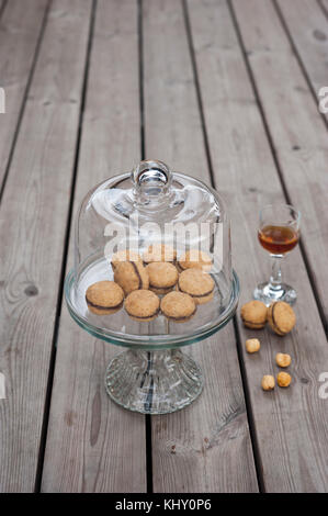 Lady's Kisses - italienische Haselnuss sandwich Cookies auf Kuchen stand mit einem Glas typisch sizilianische Likör Stockfoto