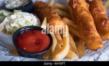 Nahaufnahme der Teller mit leckeren Fisch und Chips, Krautsalat und Salsas im englischen Stil auf einem Teller mit Zeitung Schnitten bedeckt serviert. Stockfoto