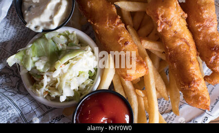 Blick von oben der leckeren Platte mit Fisch und Chips, Krautsalat und Salsas im englischen Stil auf einem Teller mit Zeitung Schnitten bedeckt serviert. Stockfoto