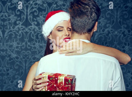 Junge Frau, die Mann an Weihnachten mit vorhanden ist, lassen Sie sich überraschen Stockfoto