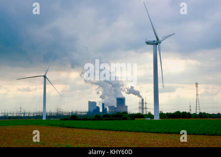 Power Generation mit alten und neuen Technologie: Wndmills im Vordergrund, braun Kohlekraftwerk im Hintergrund. Stockfoto