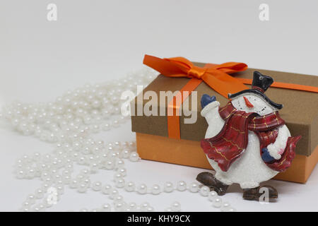 Geschenkbox mit einem orangefarbenen Bogen, weiße Perlen, Spielzeug Schneemann Stockfoto