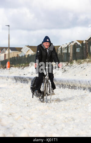 Tywyn, Großbritannien. 23 Nov, 2017. de Wetter. ein Mann Zyklen durch Sea Foam, deckt das Meer in tywyn, in der Nähe von Aberdovey, den Eindruck zu erwecken, dass es schneit wurde. Quelle: Jon Freeman/alamy leben Nachrichten Stockfoto