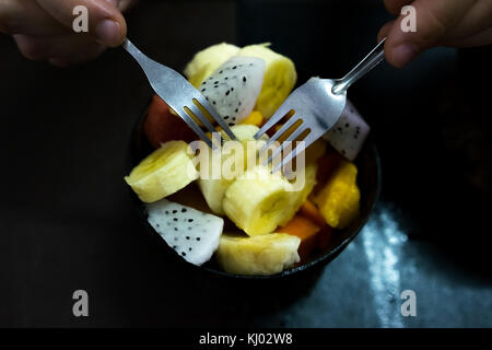 Schüssel mit gesunden Salat von frischen Früchten auf hölzernen Hintergrund. Mann es Essen mit zwei Gabeln. Stockfoto