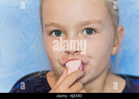 Süßes essen Mädchen mit blonden Haaren auf blauem Hintergrund Stockfoto