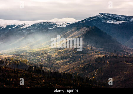 Nebel über dem Hang der Berge mit schneebedeckten Gipfel. Atemberaubende Landschaft im späten Herbst Stockfoto