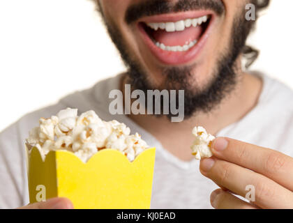 Bärtiger Mann isst Popcorn und hält einen gelben Paket in seiner Hand. Stockfoto