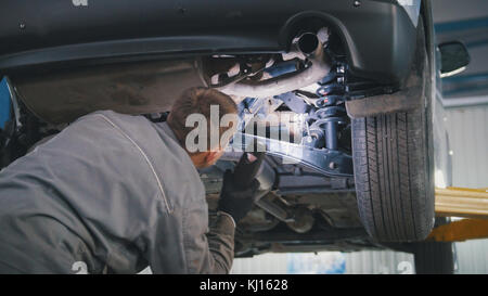 Mechaniker mit der Lampe ist die Kontrolle der Unterseite des Autos in der Garage automobile Service, Nahaufnahme Stockfoto