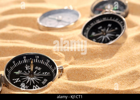 Konzeptioneller Hintergrund mit wenigen Kompasse liegen auf Sand. Bild horizontal Stockfoto