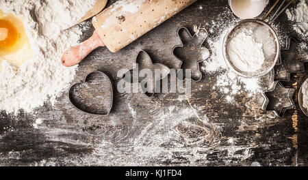 Weihnachtsbäckerei: Mehl, Eigelb, Nudelholz, Ausstecher auf dunklem Hintergrund, Ansicht von oben, Grenze Stockfoto